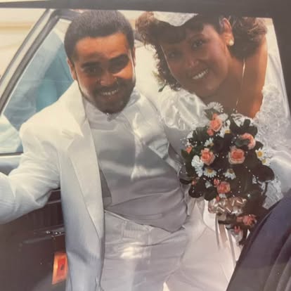 Esther and her husband smiling beside their wedding car